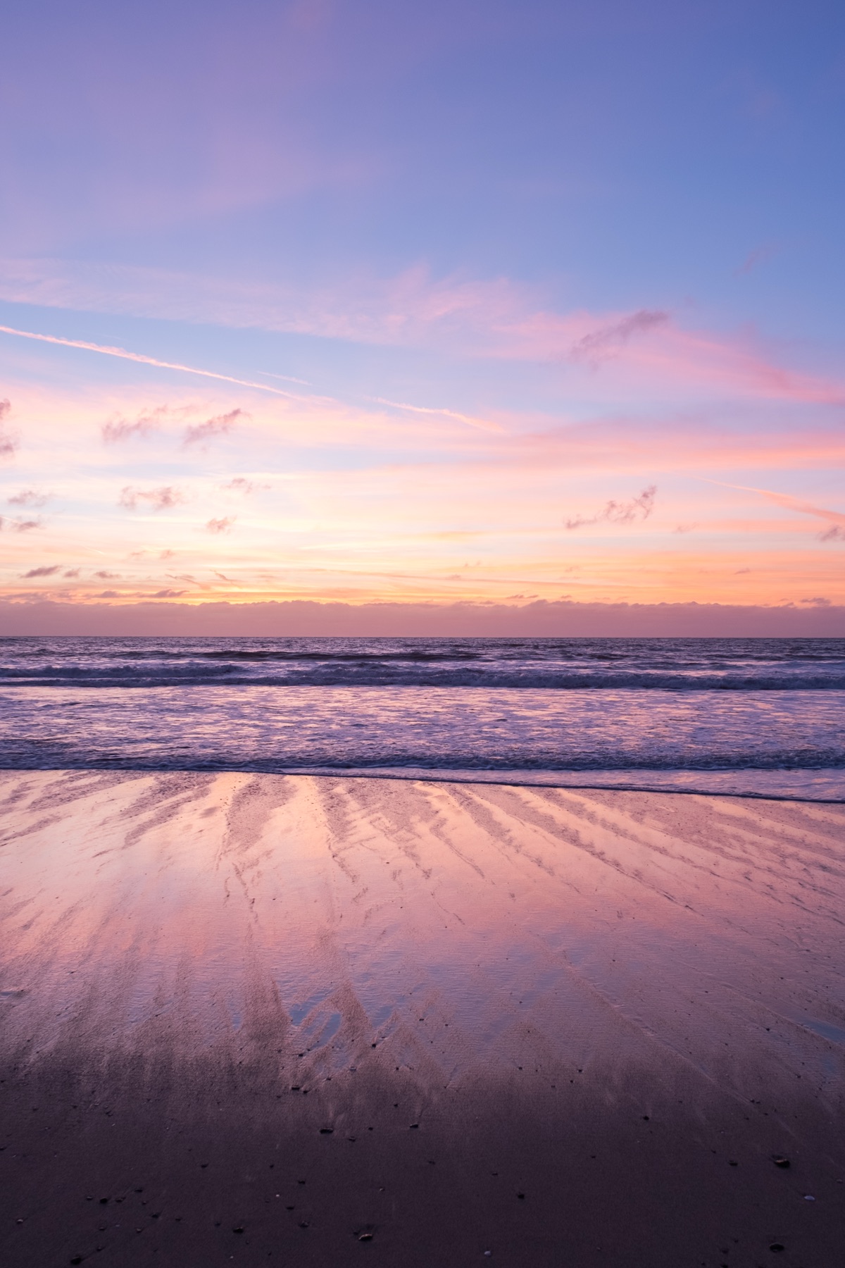 Pink and violet sunset reflected in wet sand ribbed by the outgoing tide