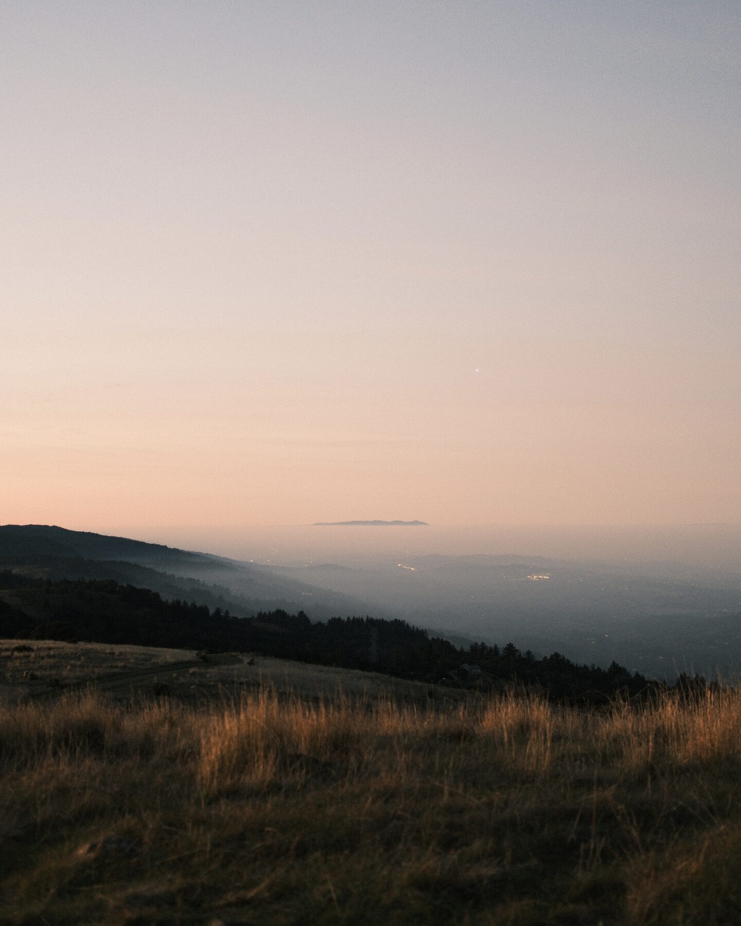 Pink dusk over dry grass and distant valley lights